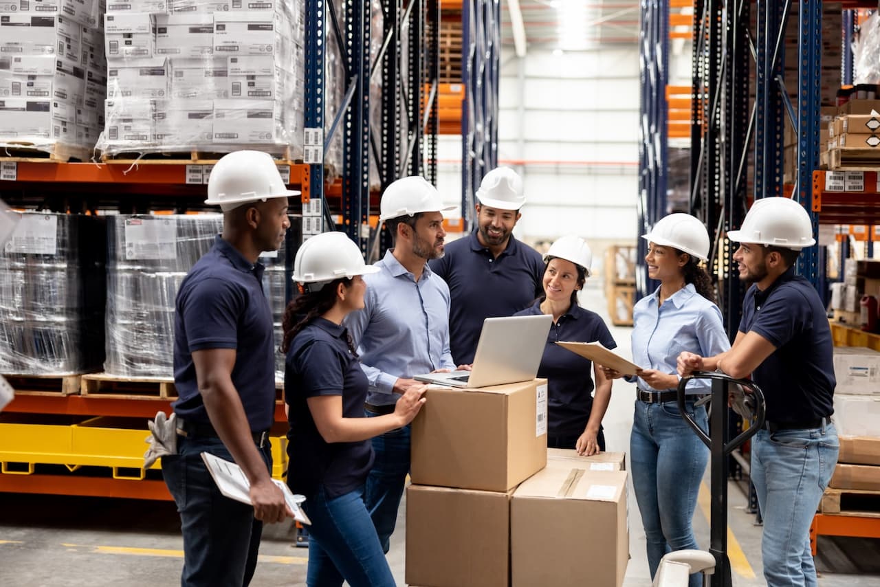 Grupo de trabajadores en una bodega discutiendo logística, un lugar donde las soluciones de Bioclimex pueden optimizar el clima laboral.